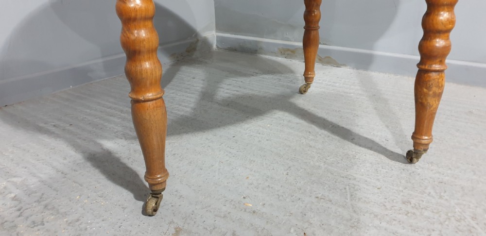 An antique round French elm dining table featuring figured wood grain, turned legs, and brass castors. View V