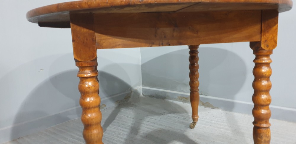 An antique round French elm dining table featuring figured wood grain, turned legs, and brass castors. View VI