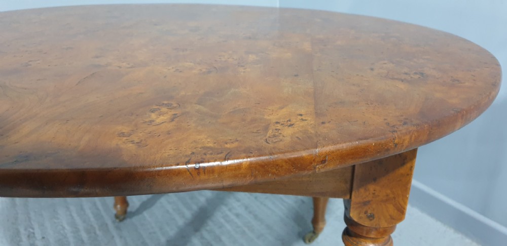 An antique round French elm dining table featuring figured wood grain, turned legs, and brass castors. View VII
