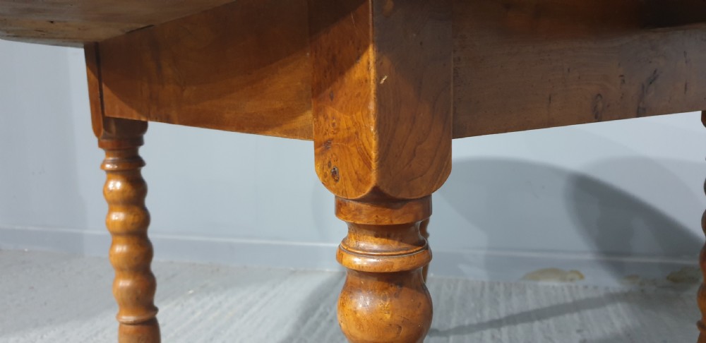 An antique round French elm dining table featuring figured wood grain, turned legs, and brass castors. View VIII