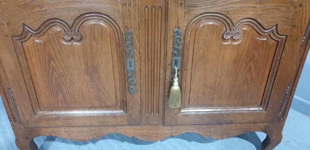 A French provincial oak dresser base featuring two carved arched cupboard doors, ornate metal keyhole hardware with a tassel, and short cabriole legs. View III