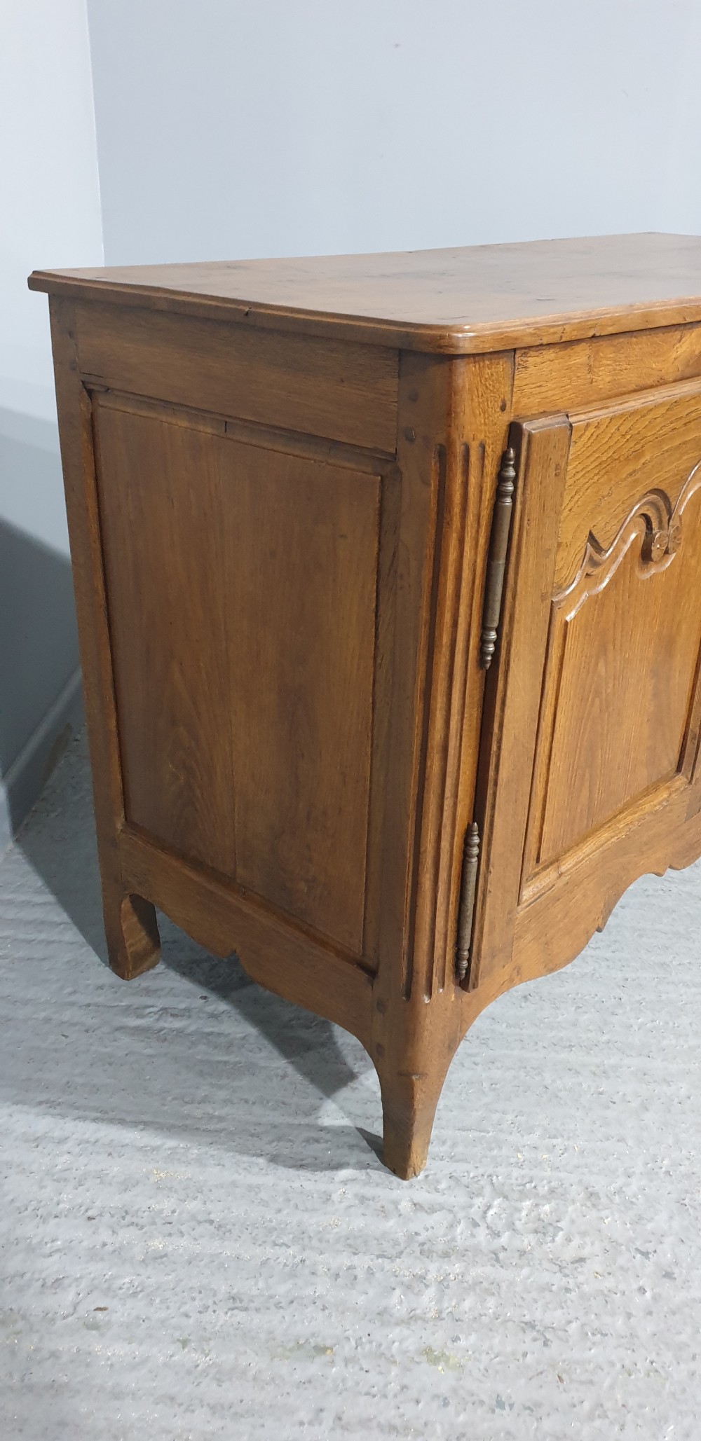 A French provincial oak dresser base featuring two carved arched cupboard doors, ornate metal keyhole hardware with a tassel, and short cabriole legs. View V