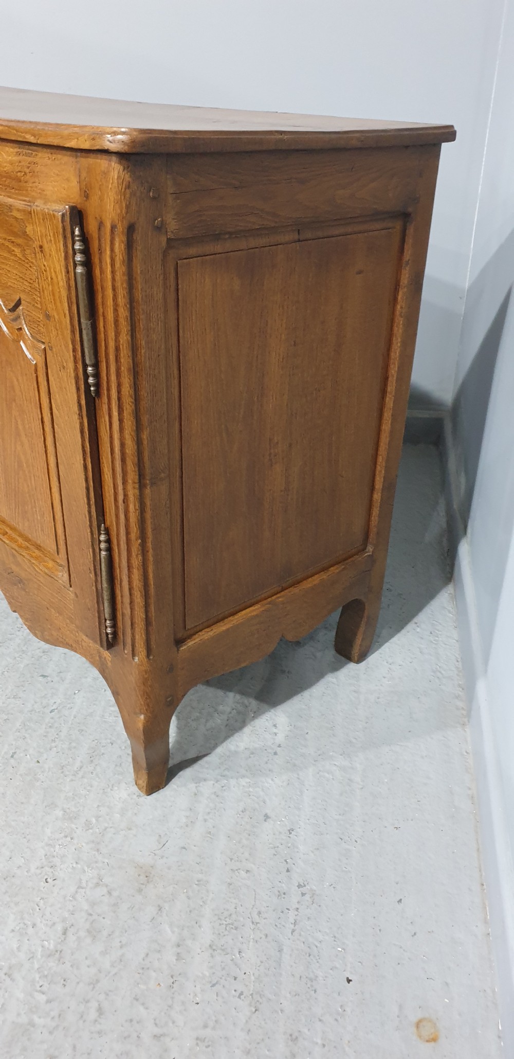A French provincial oak dresser base featuring two carved arched cupboard doors, ornate metal keyhole hardware with a tassel, and short cabriole legs. View VI