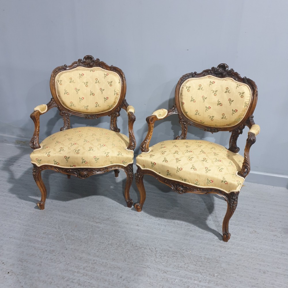 A pair of French carved mahogany open armchairs upholstered in patterned yellow floral fabric with cabriole legs.