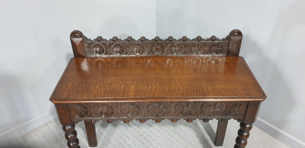 A dark carved oak console table featuring bobbin-turned front legs, a carved rosette frieze, and a low decorative gallery upstand. View II