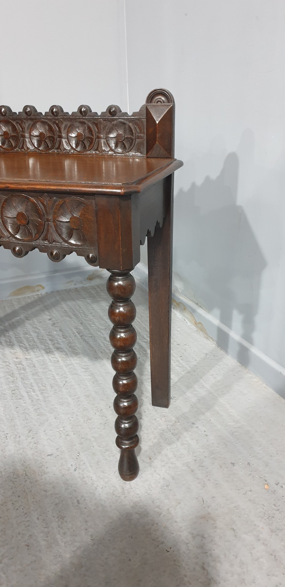 A dark carved oak console table featuring bobbin-turned front legs, a carved rosette frieze, and a low decorative gallery upstand. View III