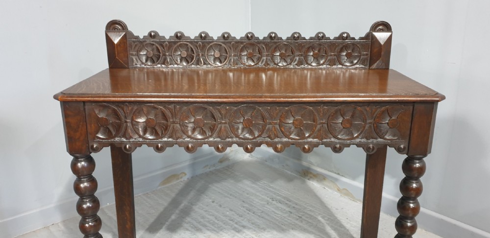 A dark carved oak console table featuring bobbin-turned front legs, a carved rosette frieze, and a low decorative gallery upstand. View IV