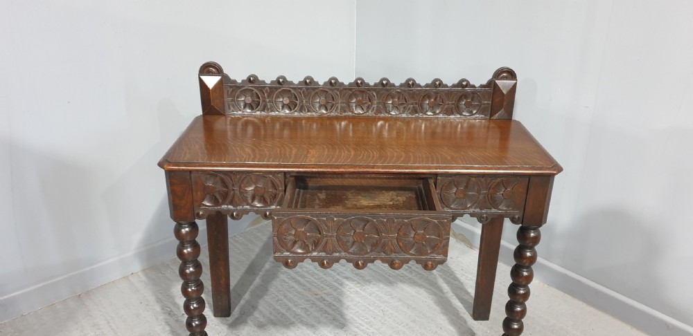 A dark carved oak console table featuring bobbin-turned front legs, a carved rosette frieze, and a low decorative gallery upstand. View V