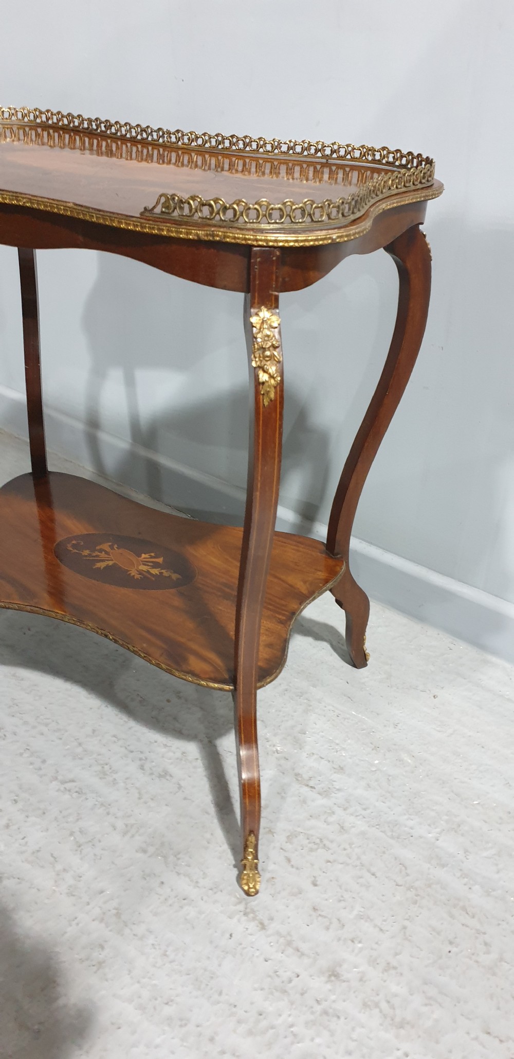 A French-style two-tier occasional table featuring marquetry wood inlays, cabriole legs, brass corner mounts, and a pierced brass gallery rim around the top surface. View V