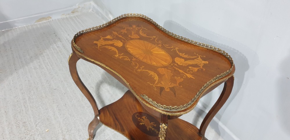 A French-style two-tier occasional table featuring marquetry wood inlays, cabriole legs, brass corner mounts, and a pierced brass gallery rim around the top surface. View VI