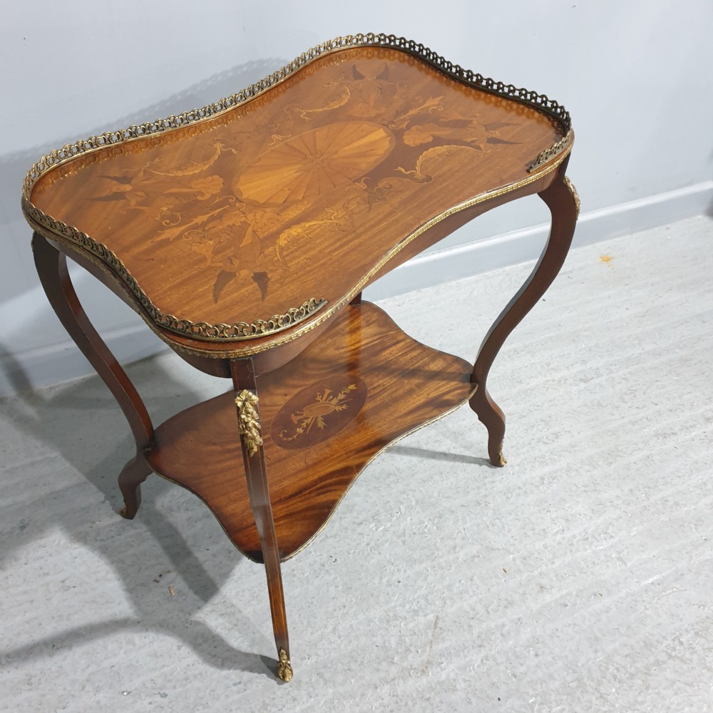 A French-style two-tier occasional table featuring marquetry wood inlays, cabriole legs, brass corner mounts, and a pierced brass gallery rim around the top surface.