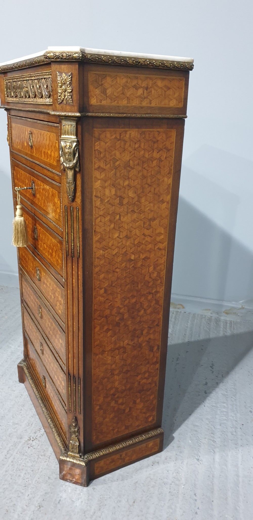 A tall French seven-drawer semainier chest with geometric wood parquetry, gold-toned ornamental mounts, and a white marble top. View III