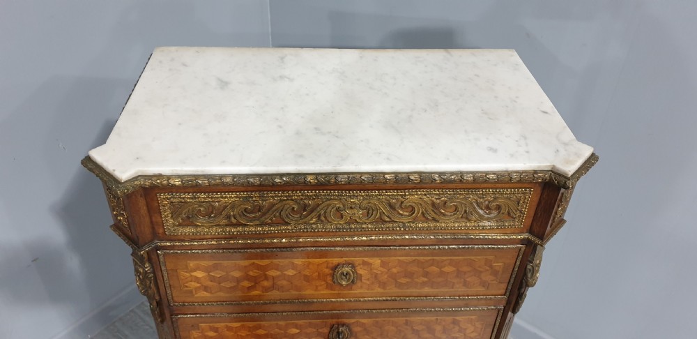 A tall French seven-drawer semainier chest with geometric wood parquetry, gold-toned ornamental mounts, and a white marble top. View VIII