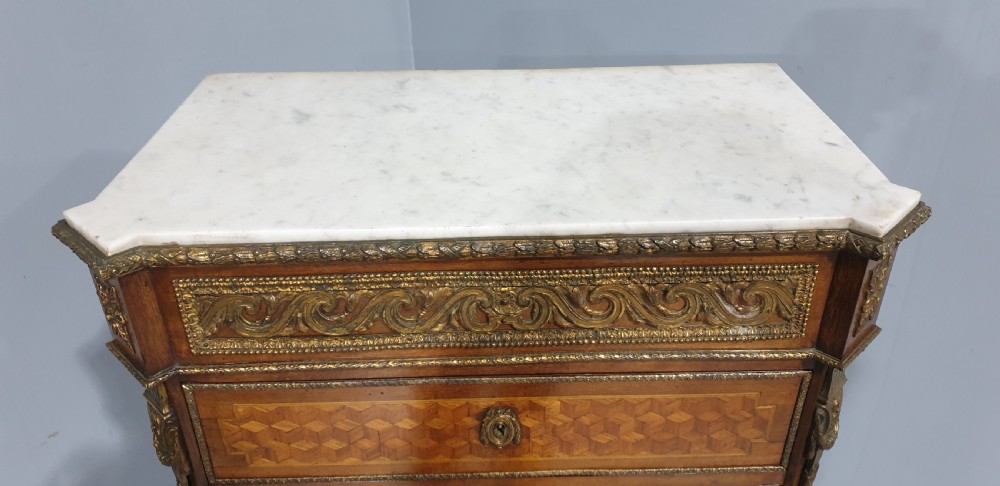 A tall French seven-drawer semainier chest with geometric wood parquetry, gold-toned ornamental mounts, and a white marble top. View XI