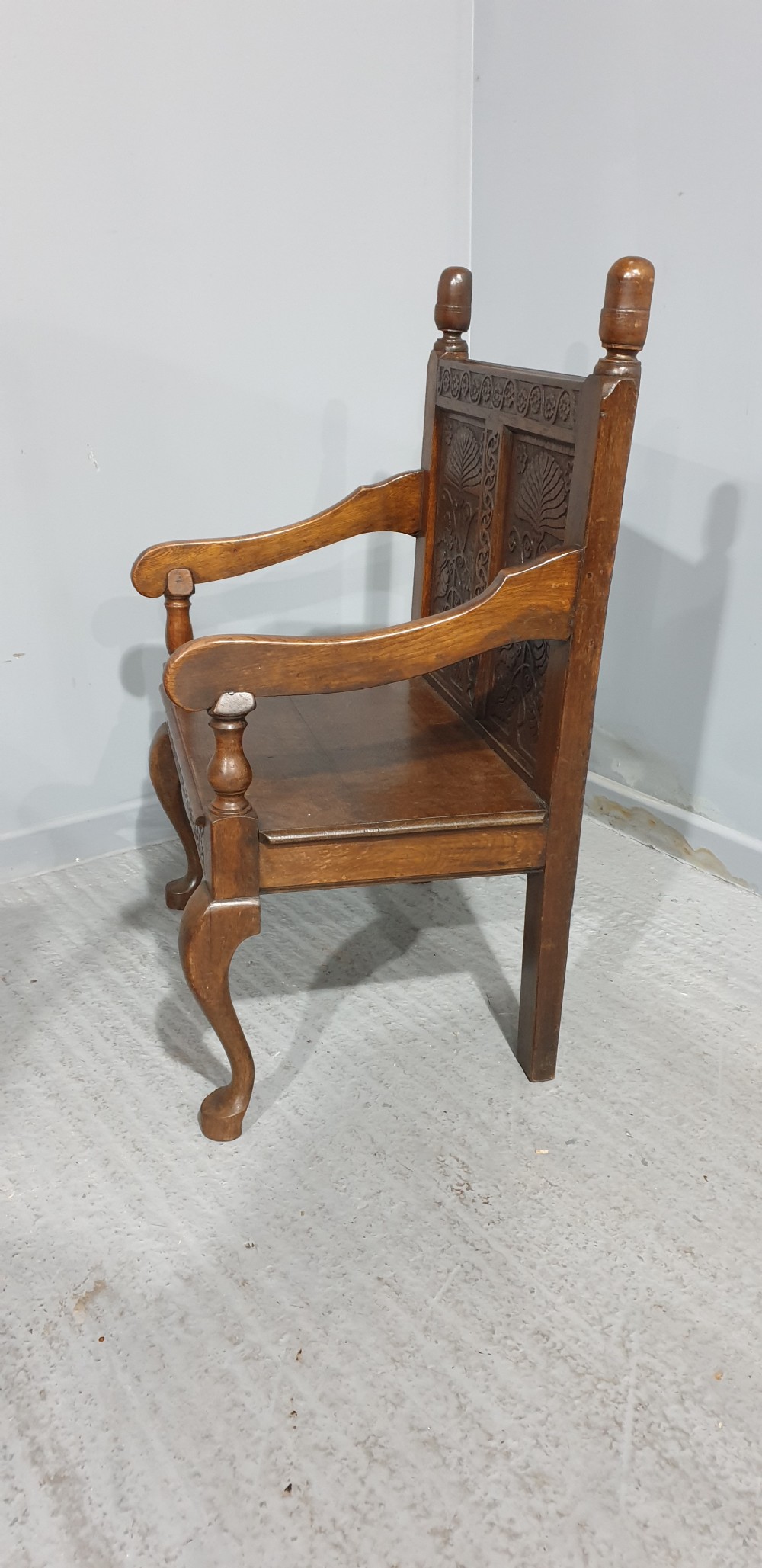 A small carved oak settle featuring a floral relief panelled back, turned finials, shaped armrests, and cabriole front legs. View II