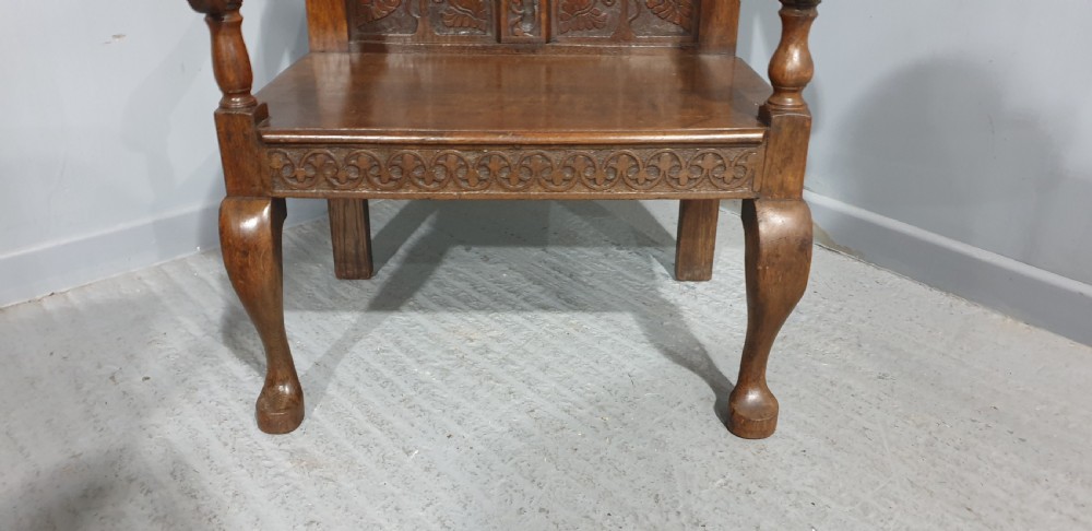 A small carved oak settle featuring a floral relief panelled back, turned finials, shaped armrests, and cabriole front legs. View V