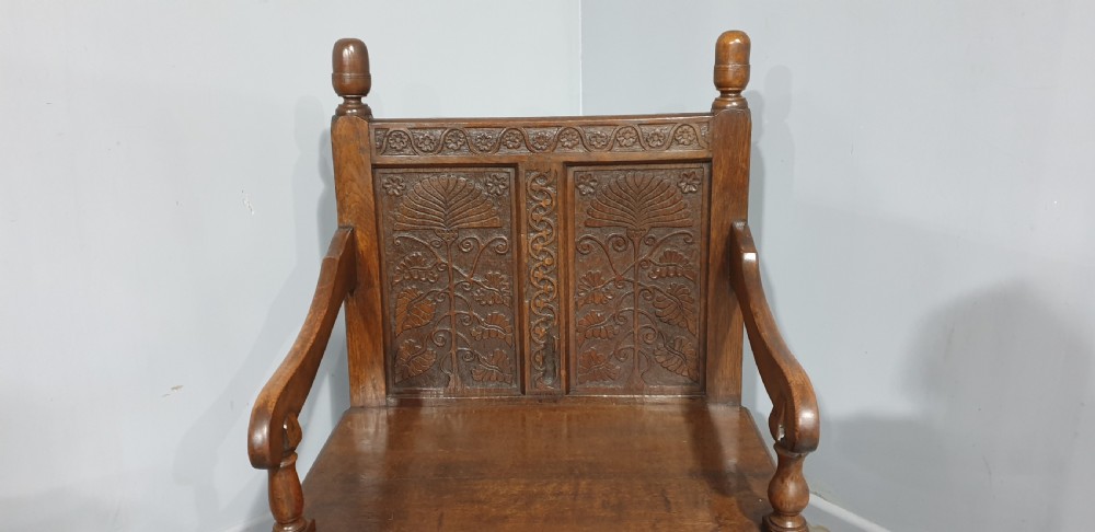A small carved oak settle featuring a floral relief panelled back, turned finials, shaped armrests, and cabriole front legs. View VI