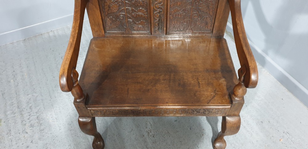 A small carved oak settle featuring a floral relief panelled back, turned finials, shaped armrests, and cabriole front legs. View IX