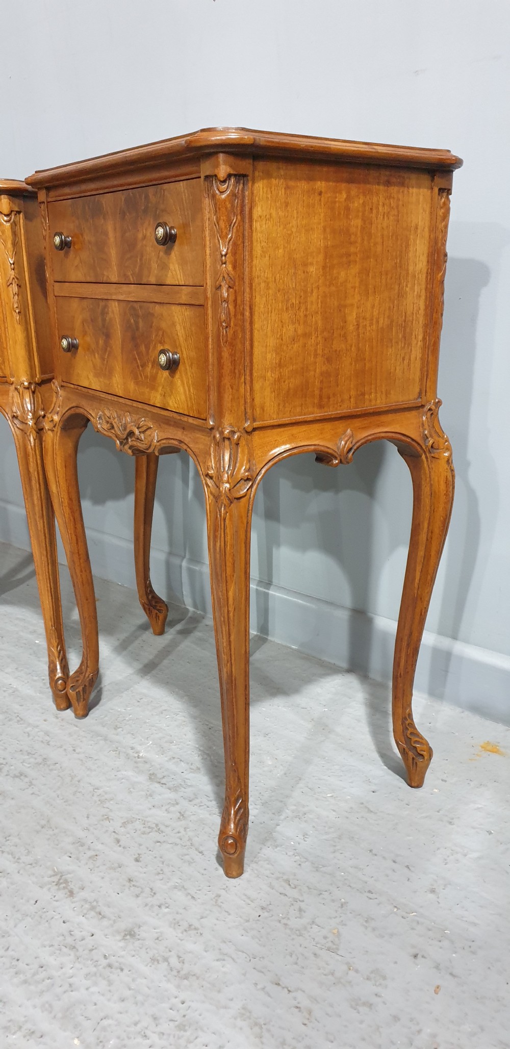 A pair of warm brown walnut bedside chests featuring two drawers with brass knobs, carved aprons, and long cabriole legs. View VII