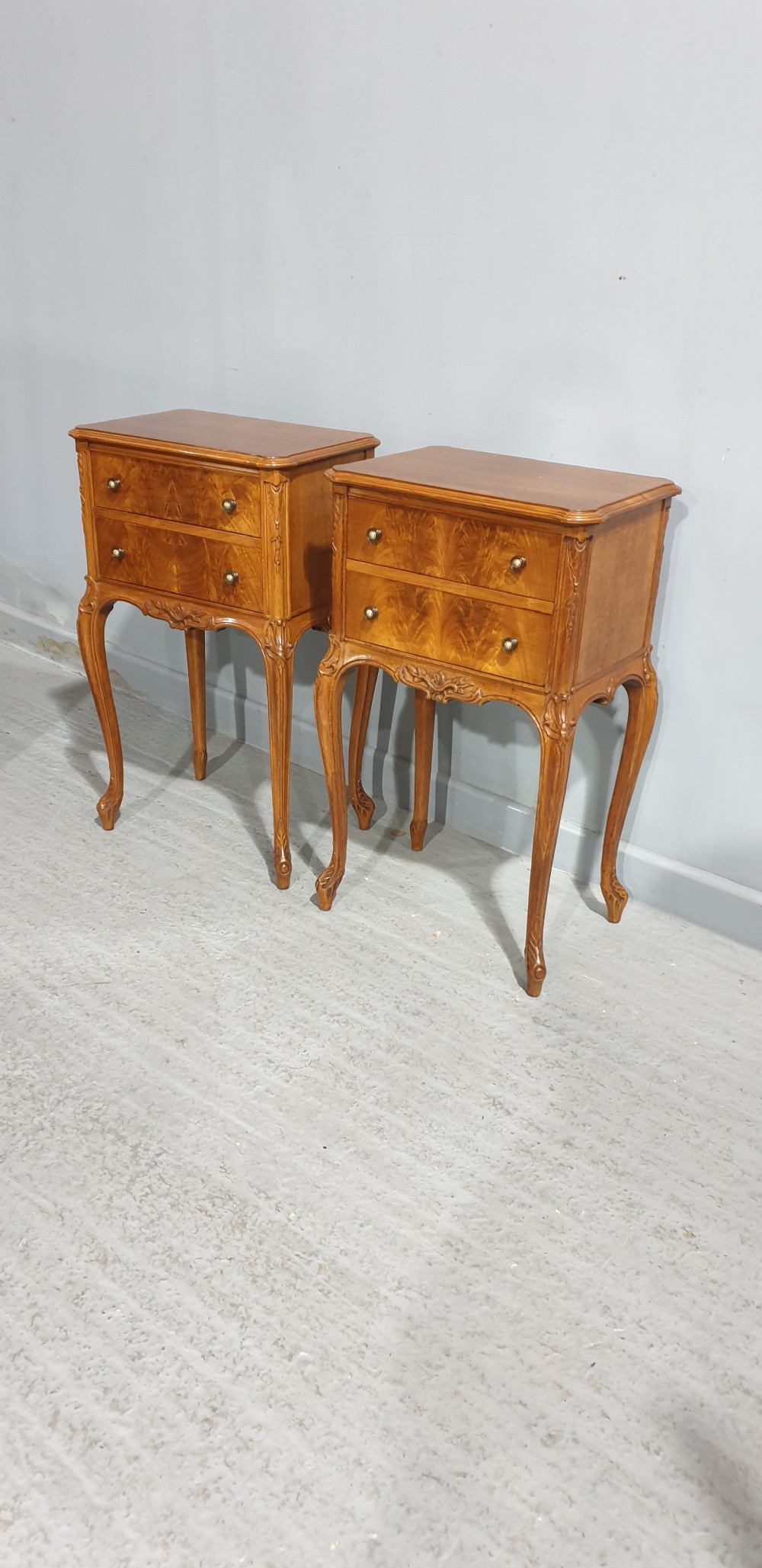 A pair of warm brown walnut bedside chests featuring two drawers with brass knobs, carved aprons, and long cabriole legs. View IX