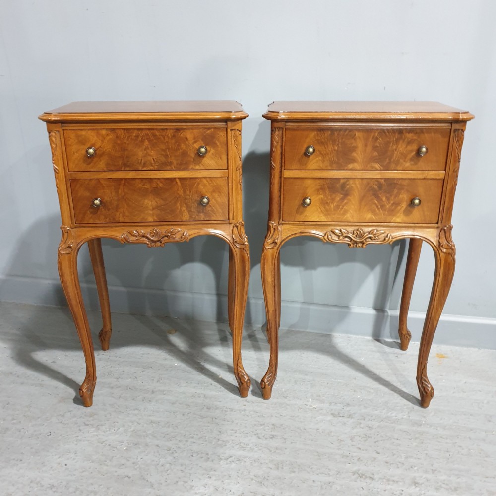 A pair of warm brown walnut bedside chests featuring two drawers with brass knobs, carved aprons, and long cabriole legs.