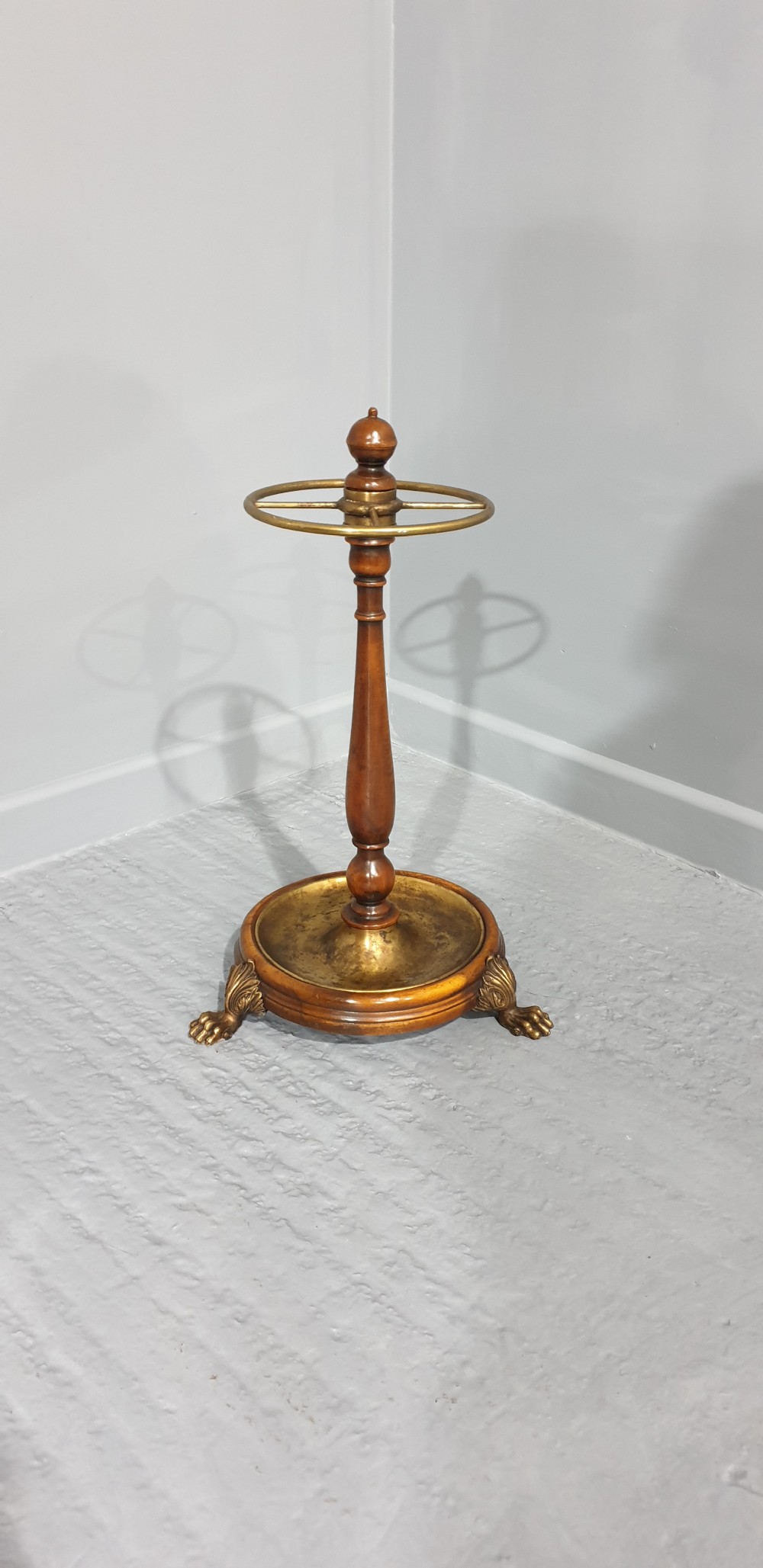 A Victorian turned mahogany stick stand featuring a circular top brass divider ring, a central turned stem, and a round brass drip tray base elevated by brass claw feet. View III