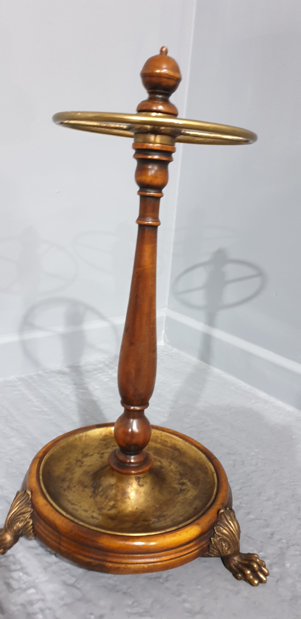 A Victorian turned mahogany stick stand featuring a circular top brass divider ring, a central turned stem, and a round brass drip tray base elevated by brass claw feet. View IV