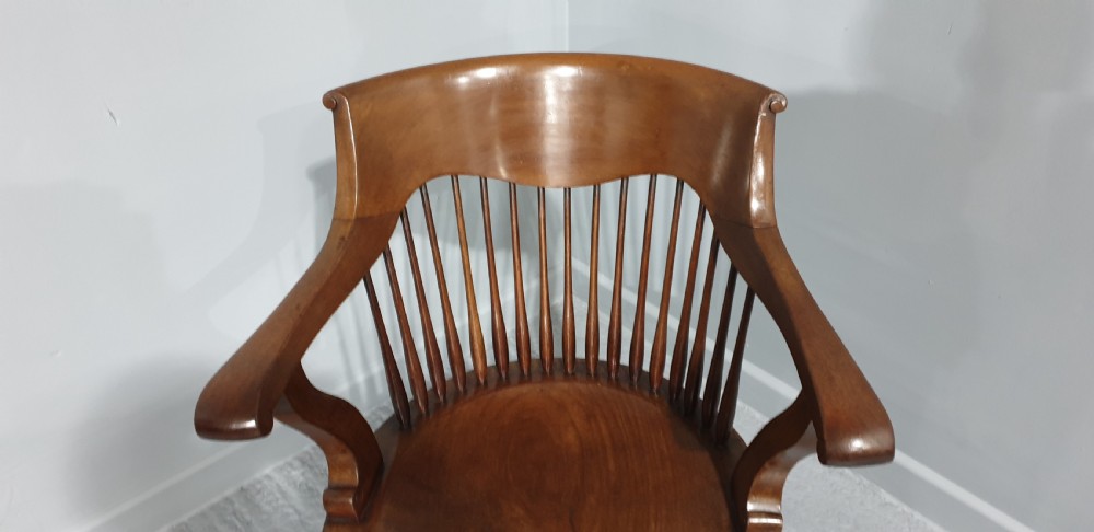 An antique mahogany desk armchair featuring a curved crest rail, vertical spindle back, contoured wooden seat, and shaped front legs. View III