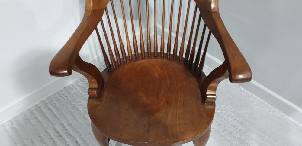 An antique mahogany desk armchair featuring a curved crest rail, vertical spindle back, contoured wooden seat, and shaped front legs. View V