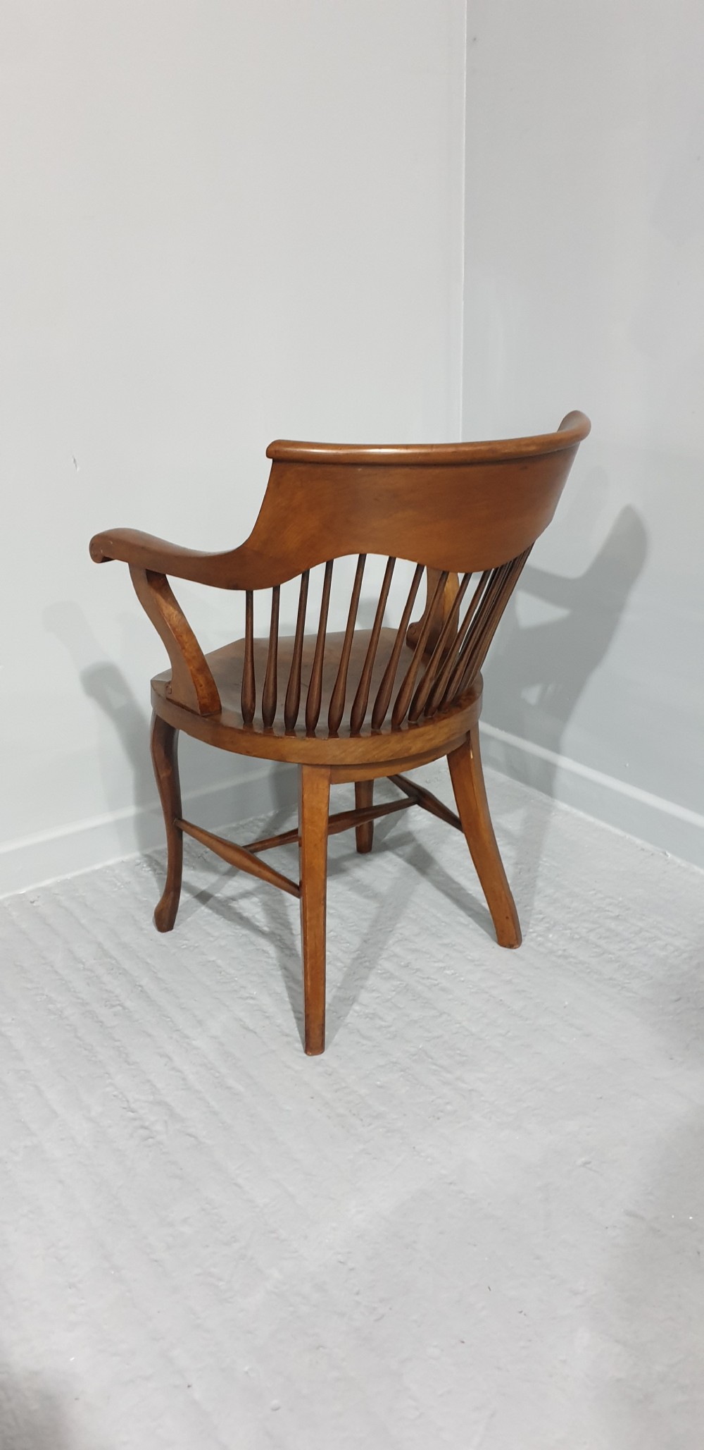 An antique mahogany desk armchair featuring a curved crest rail, vertical spindle back, contoured wooden seat, and shaped front legs. View VI
