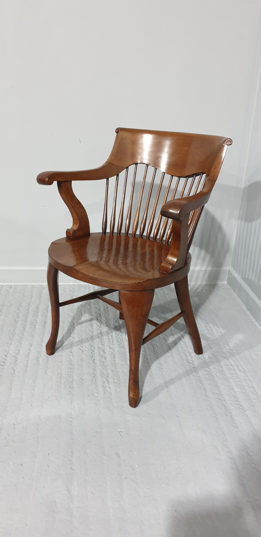An antique mahogany desk armchair featuring a curved crest rail, vertical spindle back, contoured wooden seat, and shaped front legs. View VII