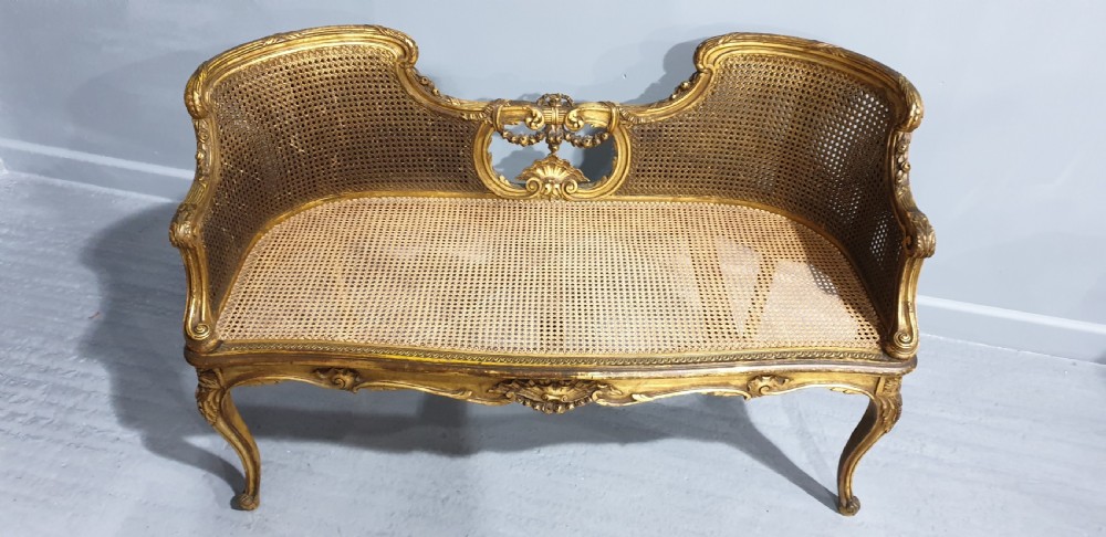 A Louis XV style French giltwood two-seater window bench featuring carved Rococo cartouches, cabriole legs, and natural woven cane panels. View II