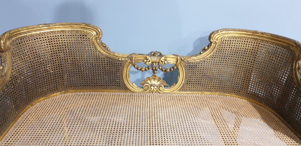 A Louis XV style French giltwood two-seater window bench featuring carved Rococo cartouches, cabriole legs, and natural woven cane panels. View III