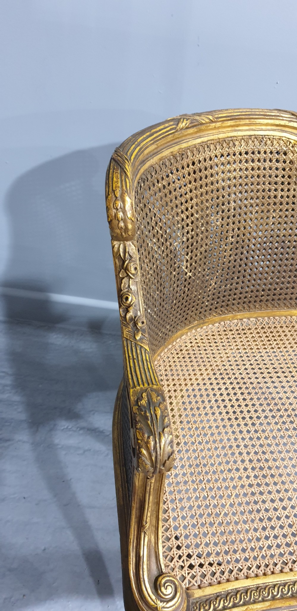 A Louis XV style French giltwood two-seater window bench featuring carved Rococo cartouches, cabriole legs, and natural woven cane panels. View VI