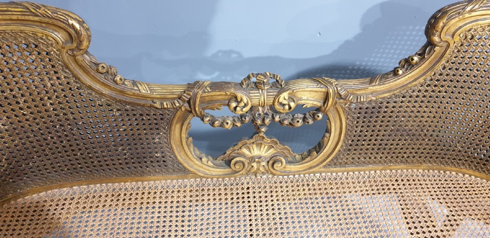 A Louis XV style French giltwood two-seater window bench featuring carved Rococo cartouches, cabriole legs, and natural woven cane panels. View VII
