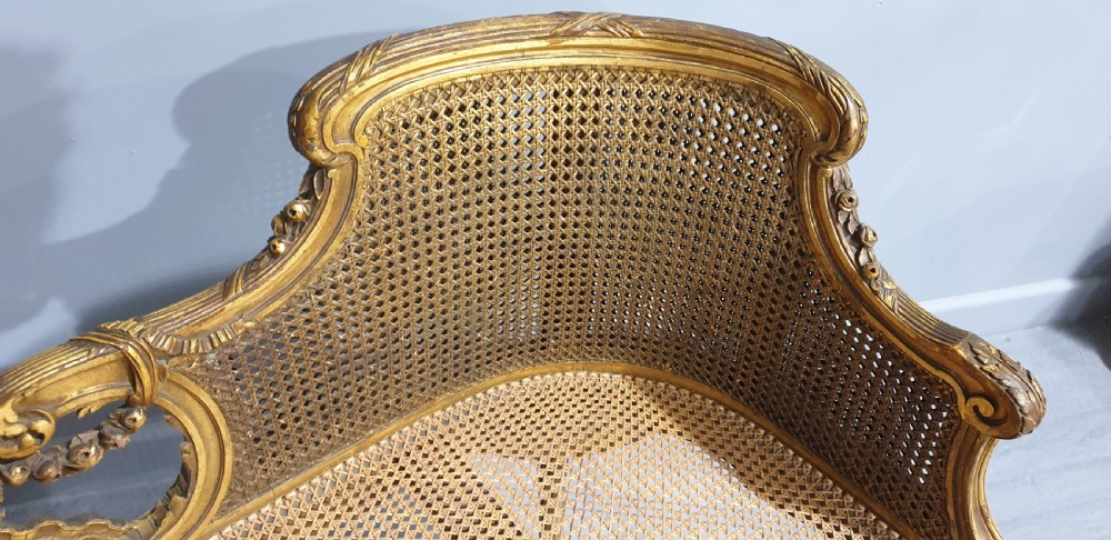 A Louis XV style French giltwood two-seater window bench featuring carved Rococo cartouches, cabriole legs, and natural woven cane panels. View VIII