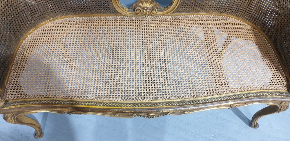 A Louis XV style French giltwood two-seater window bench featuring carved Rococo cartouches, cabriole legs, and natural woven cane panels. View IX