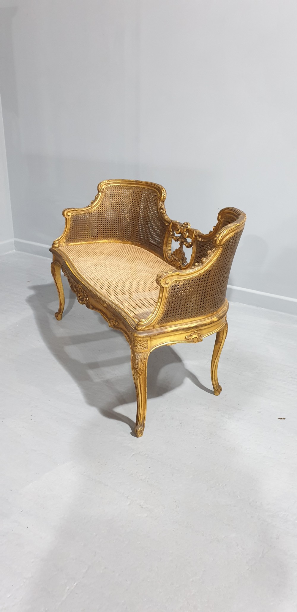 A Louis XV style French giltwood two-seater window bench featuring carved Rococo cartouches, cabriole legs, and natural woven cane panels. View XI