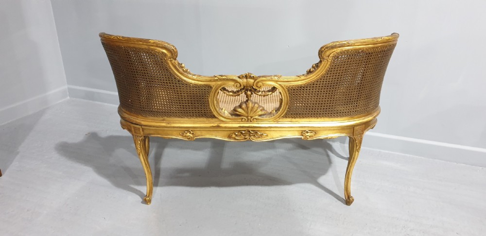 A Louis XV style French giltwood two-seater window bench featuring carved Rococo cartouches, cabriole legs, and natural woven cane panels. View XII