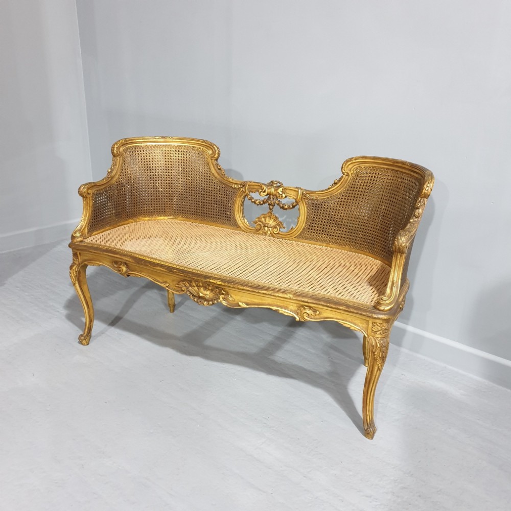 A Louis XV style French giltwood two-seater window bench featuring carved Rococo cartouches, cabriole legs, and natural woven cane panels.