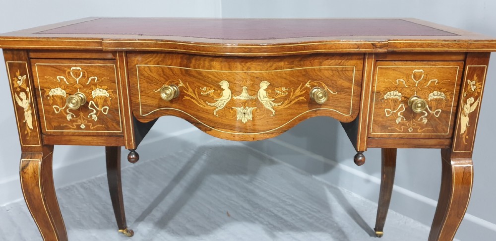 An antique rosewood writing desk featuring floral marquetry inlays, a red leather inset top, three drawers, and slender cabriole legs on brass castors. View III