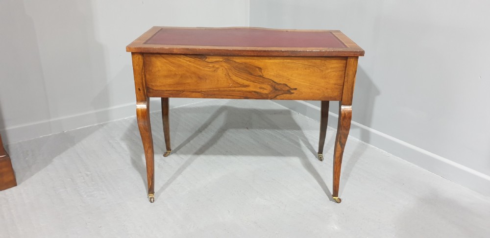 An antique rosewood writing desk featuring floral marquetry inlays, a red leather inset top, three drawers, and slender cabriole legs on brass castors. View IX