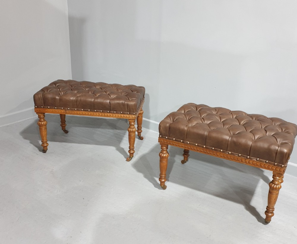 A pair of Victorian deep-buttoned brown leather window seats featuring carved turned legs on brass castors with brass stud detailing.