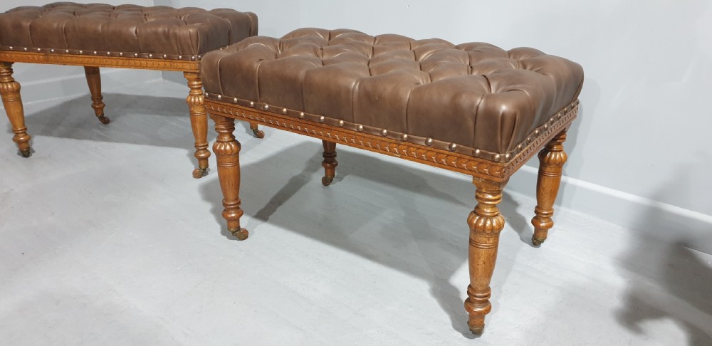A pair of Victorian deep-buttoned brown leather window seats featuring carved turned legs on brass castors with brass stud detailing. View IV