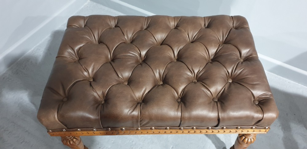 A pair of Victorian deep-buttoned brown leather window seats featuring carved turned legs on brass castors with brass stud detailing. View V