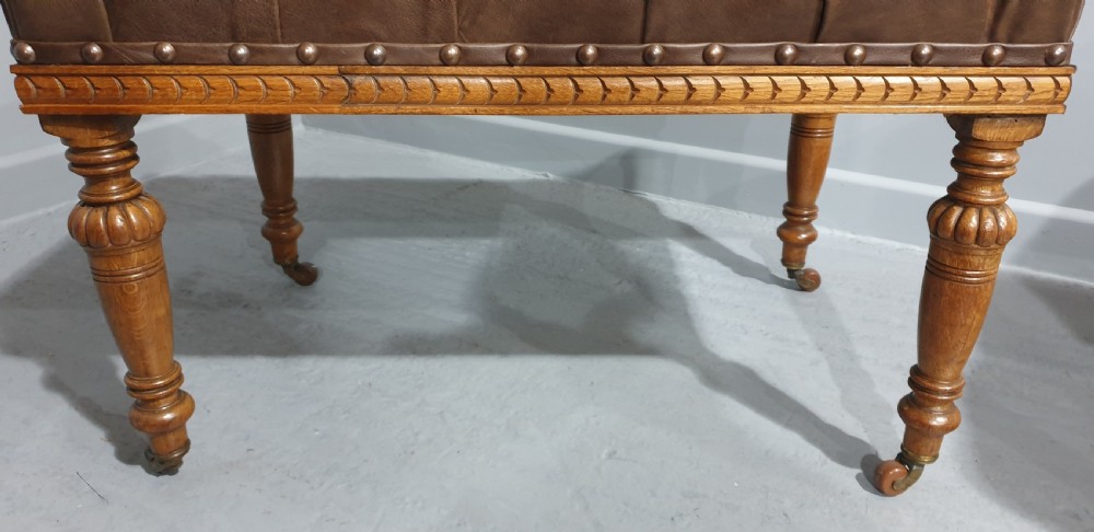 A pair of Victorian deep-buttoned brown leather window seats featuring carved turned legs on brass castors with brass stud detailing. View VII