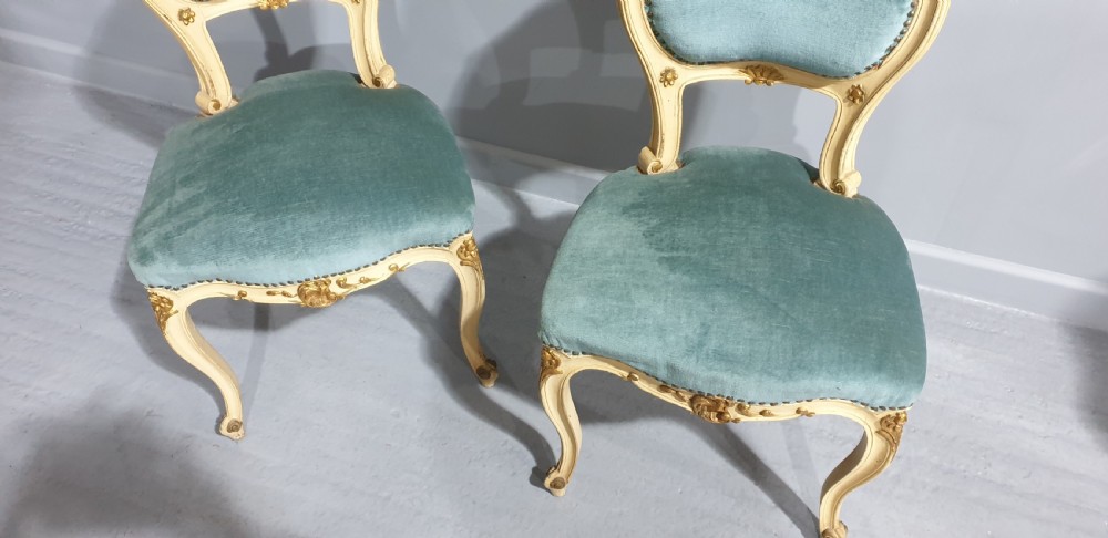 A pair of French Rococo style side chairs featuring cream and gold painted wooden frames with cabriole legs and blue velvet upholstery. View V