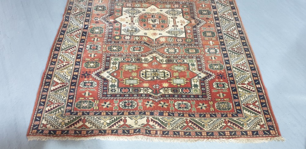 A large hand-knotted Persian wool area rug featuring central geometric medallions in terracotta red, navy blue, green, and cream. View III