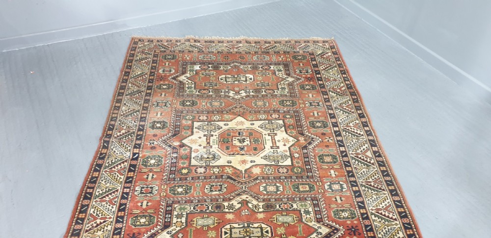 A large hand-knotted Persian wool area rug featuring central geometric medallions in terracotta red, navy blue, green, and cream. View V