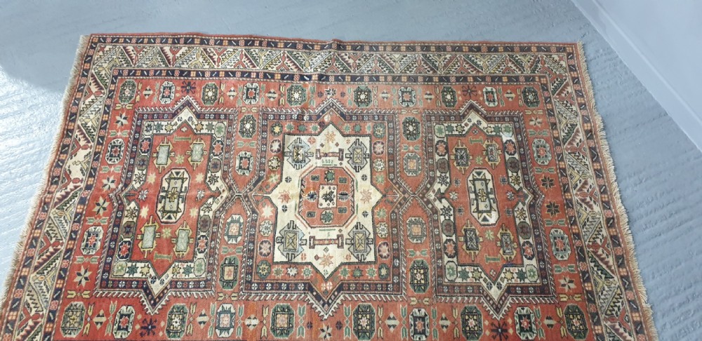A large hand-knotted Persian wool area rug featuring central geometric medallions in terracotta red, navy blue, green, and cream. View VI